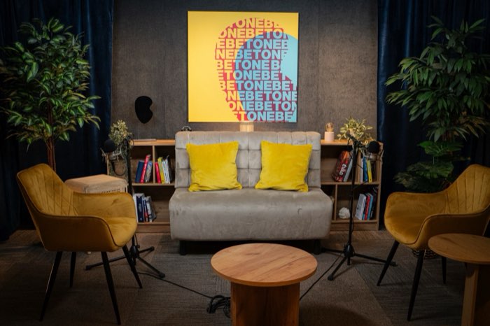 Studio 1 from the front: a sofa with yellow cushions, two mustard armchairs and two microphones.