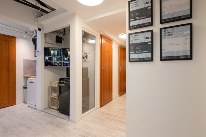 The corridor and kitchenette, with a screen showing the camera feeds and framed certificates on the wall.