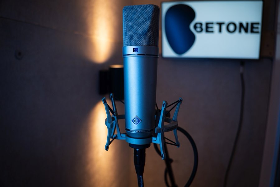 Close-up of a Neumann U87 microphone in the voiceover booth, with the Betone logo on a screen behind it.